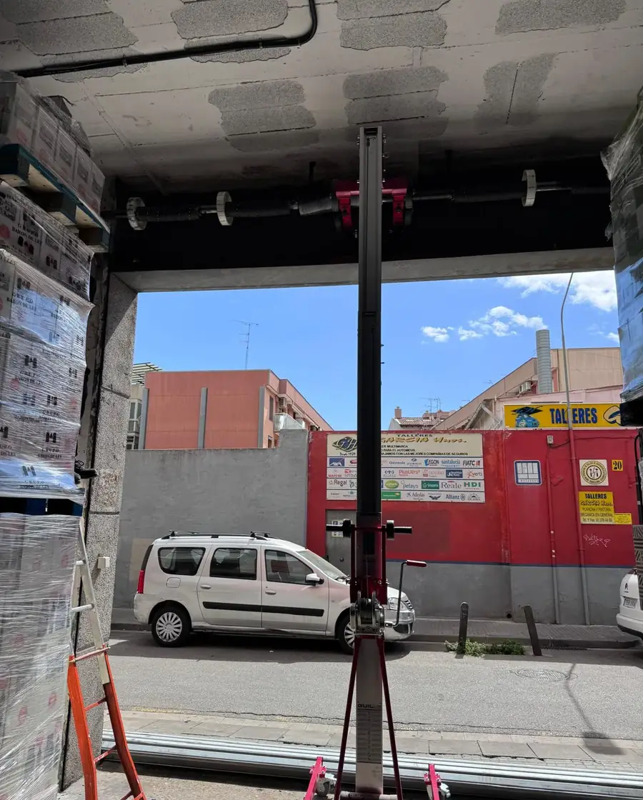 Eje de una persiana metálica siendo montado con un elevador hidráulico en el acceso de un almacén